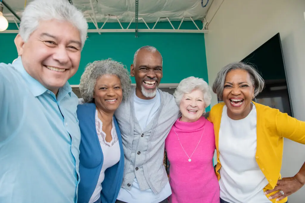 A group of older adults smile and hug while standing in a large room