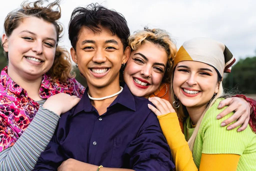 A group of diverse adolescents hug and smile outdoors