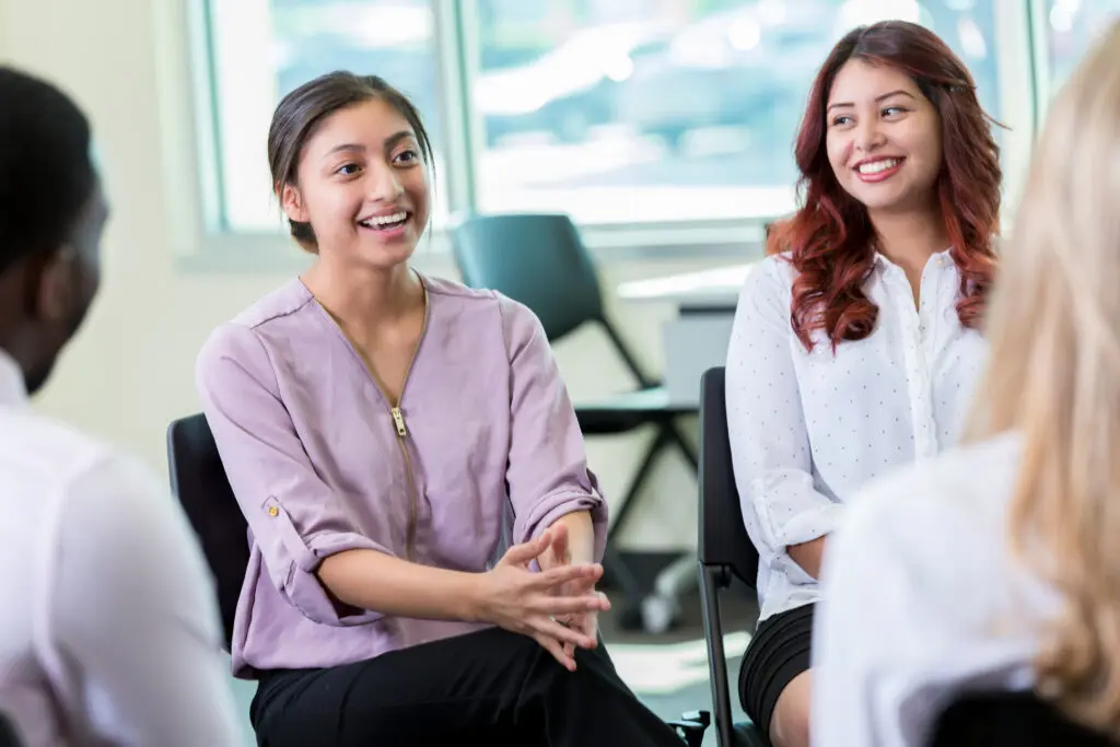 A group of adult women sit in a circle as they participate group therapy