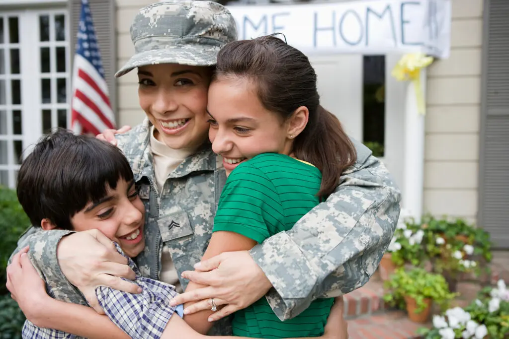 A mother in her military uniform is welcomed home with a hug from her two children